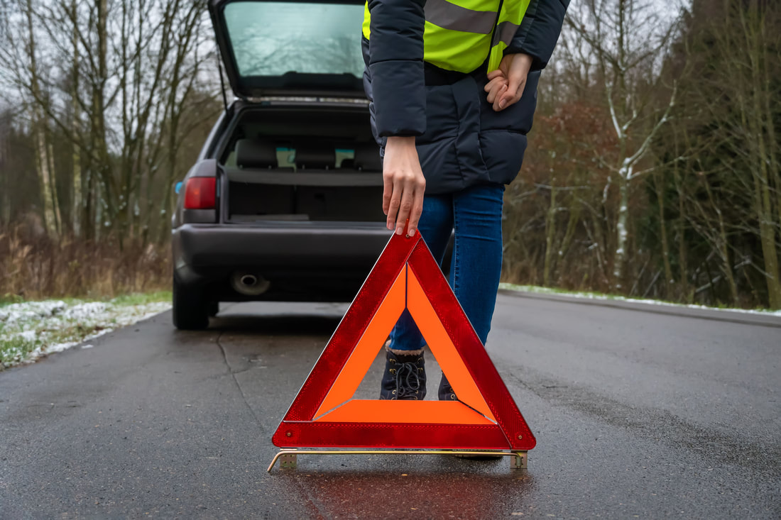 Woman placing orange triangle road hazard sign behind her car
