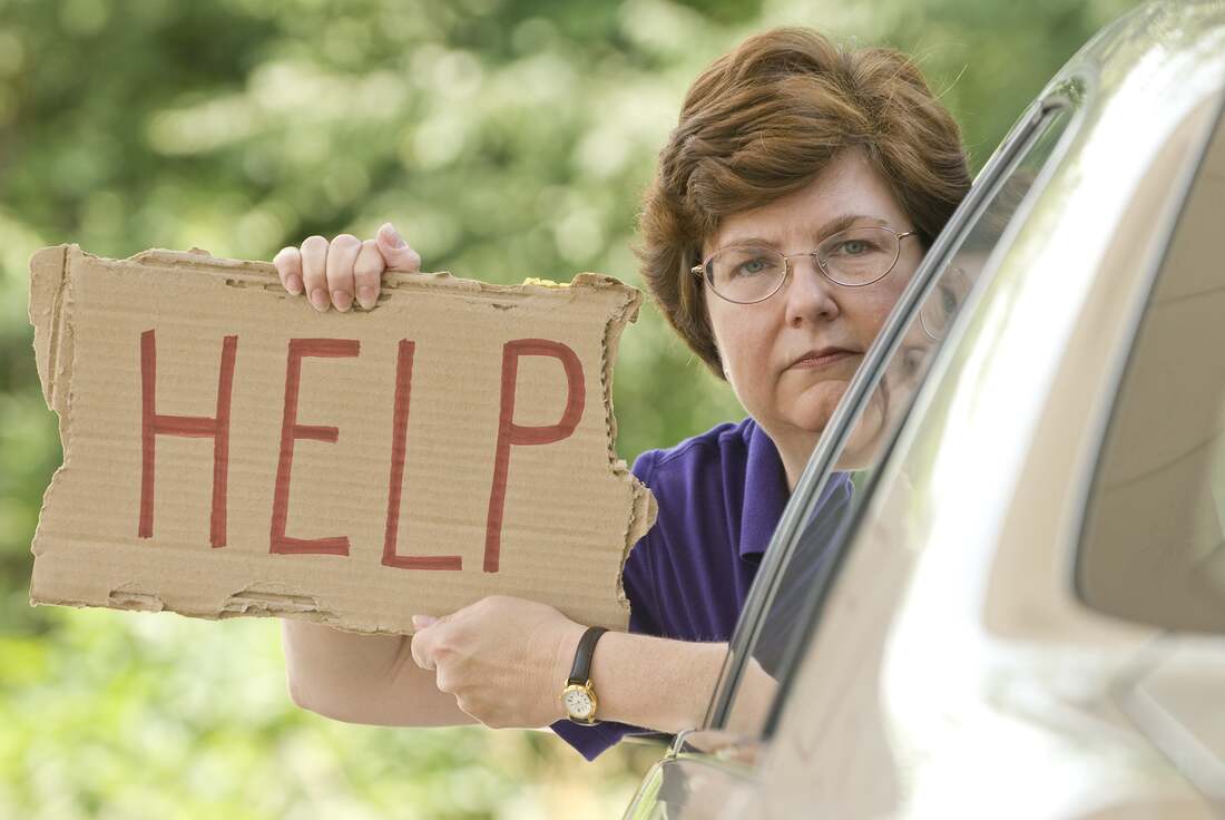 Woman stranded in car on side of the road holding Help sign out of the window